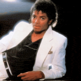 a man wearing a white jacket and a black shirt is sitting down