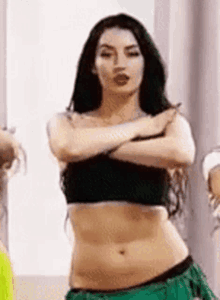 a woman in a black top and green skirt is dancing belly dance with her arms crossed .