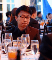 a man with glasses sits at a table with glasses of water