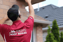 a man wearing a toronto roof repairs shirt hangs from a brick wall