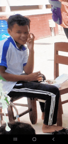 a young boy is sitting on a wooden chair with a plate of food in front of him