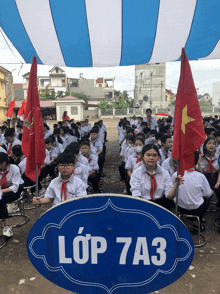 a group of students are sitting under a blue sign that says lớp 7a3