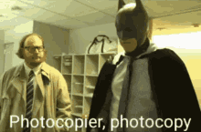 a man in a batman costume is talking to another man in a trench coat and tie