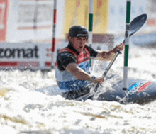 a man is paddling a kayak in a river with a zomat sign in the background .