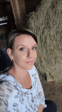 a woman taking a selfie in front of a bale of hay