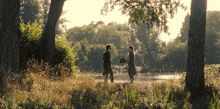 a man and a woman are standing in a field near a lake