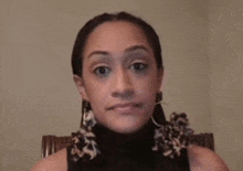 a woman wearing a black turtleneck and earrings is sitting in a chair and looking at the camera .