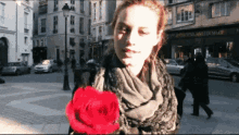 a woman in a scarf is holding a red rose in front of a building that says ' avenue de la mairie '