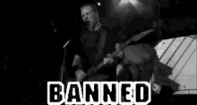 a black and white photo of a man playing a guitar and singing into a microphone with the words banned in white letters .