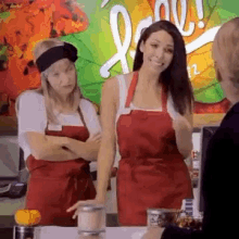 two women wearing red aprons are standing next to each other in front of a sign that says " love "