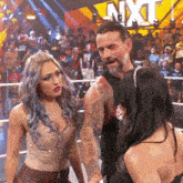 a man and two women are standing in front of a sign that says nxt on it