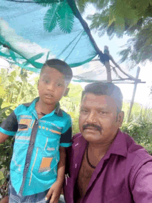 a man in a purple shirt poses for a picture with a boy in a blue shirt