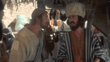 a man with a beard and a striped robe is talking to another man