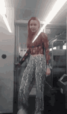 a woman wearing a crop top and snake print pants is standing in a train car