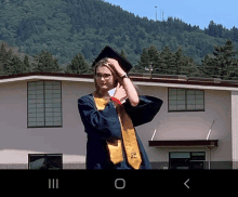 a woman in a graduation cap and gown is adjusting her cap in front of a building