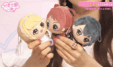 a woman holds three stuffed dolls in her hands with chinese writing on the bottom right