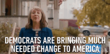 a woman is standing in front of a house holding a broom and says democrats are bringing much needed change to america