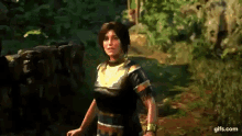 a woman in a black and gold dress is standing in a forest .