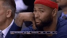 a man wearing a red headband is sitting in the stands watching a basketball game between new orleans and charlotte