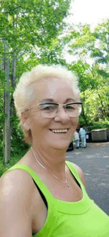 an older woman wearing glasses and a green tank top is smiling .