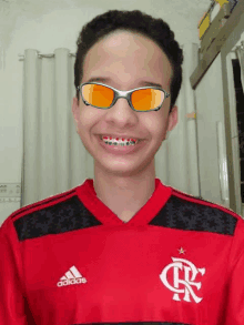 a boy wearing braces and sunglasses is wearing an adidas shirt