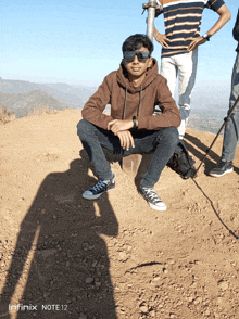 a man wearing sunglasses sits on top of a dirt hill with the infinity note 12 in the background