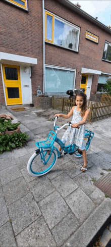 a little girl is riding a blue bicycle in front of a brick house