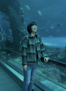 a woman stands in front of a large aquarium