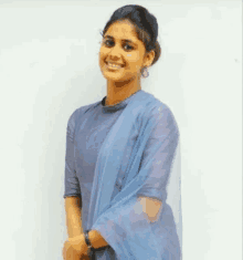 a young woman wearing a blue dress and a blue dupatta is smiling for the camera .