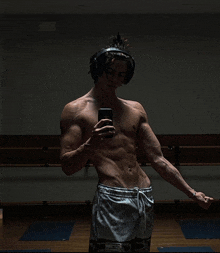 a shirtless man wearing headphones takes a selfie in a gym