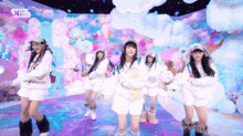 a group of girls are dancing on a stage in front of a cloudy background ..