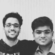 two young men are posing for a picture together in a black and white photo . one of the men is wearing glasses .