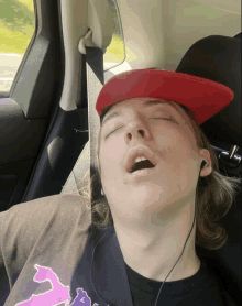 a young man wearing a red hat is sleeping in a car