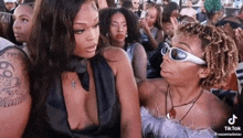 two women wearing sunglasses are talking to each other in a crowd .