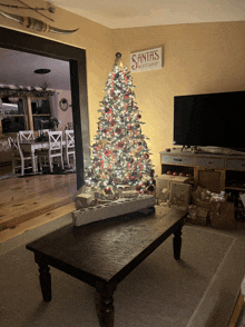 a living room with a christmas tree and a santa 's workshop sign on the wall