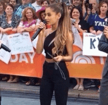 a woman singing into a microphone in front of a crowd of people holding signs that say today