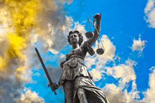 a statue of justice holding scales and a sword against a cloudy sky