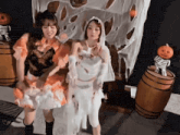 two women dressed in halloween costumes are dancing in front of a skeleton and pumpkins