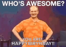 a man in an orange shirt is standing on a stage with his hands on his hips and a happy birthday message .