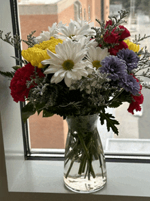 a clear vase filled with flowers sits on a window sill