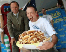 a man is holding a tray of hot dogs in front of a man in a suit and tie .