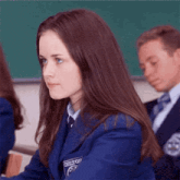 a girl in a blue school uniform is sitting at a desk in a classroom with other students .