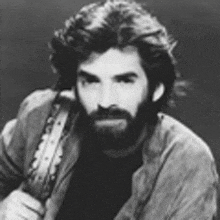 a man with a beard and long hair is holding a guitar .