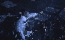 a group of people are dancing in a dark room with a man in a white feathered outfit .