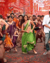 a woman in a green saree is dancing with a crowd of people .