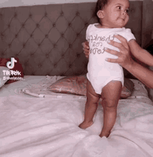 a baby is standing on a bed while being held by a woman .