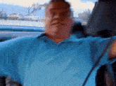 a man wearing a blue shirt is sitting in a car with his arms outstretched