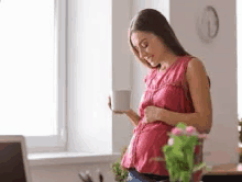 a pregnant woman is drinking a cup of coffee while standing in front of a window .