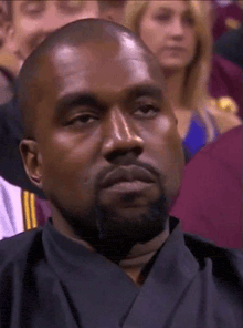 a man with a beard is sitting in a crowd of people and making a face .