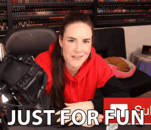 a woman in a red hoodie sits in front of a sign that says " just for fun "